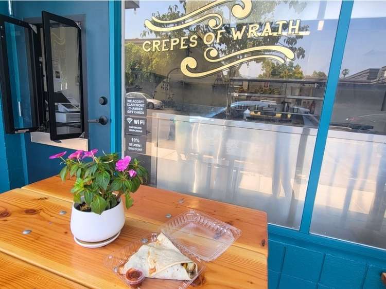 A fresh veggie crepe sits on a small wooden table in front of an order window.