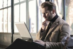 A man is working on his laptop while waiting at a station.